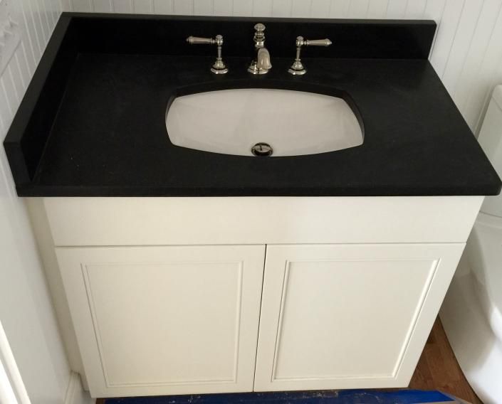 Bathroom vanity with black countertop, white sink, off-white cabinet, and silver faucet.