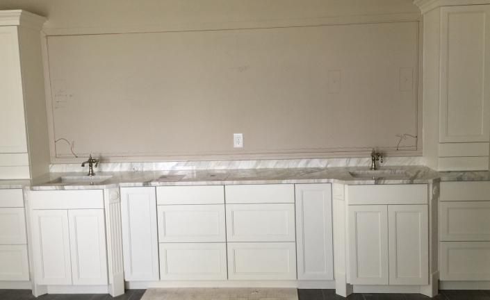 White kitchen cabinets with marble countertops and a beige wall.