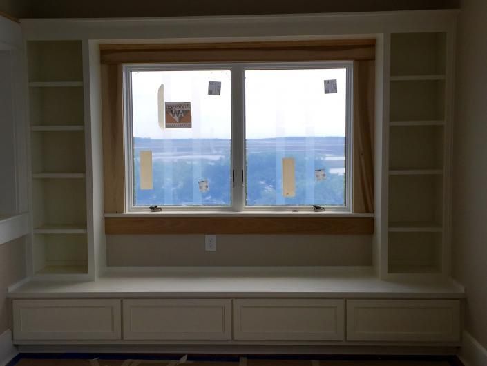 Built-in window seat with bookshelves and drawers, painted cream. A window with a view is centered.