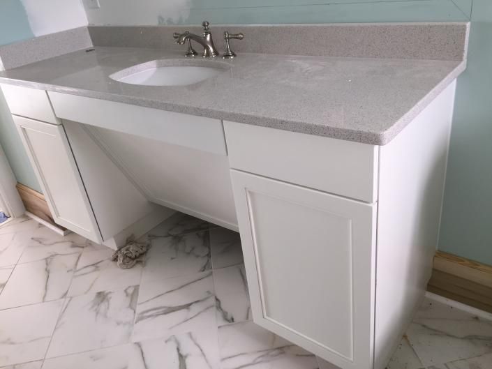 White bathroom vanity with gray countertop and silver faucet, set against a light blue wall.