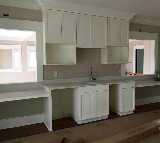 Built-in off-white cabinets with a sink. White countertops and open spaces beneath them.