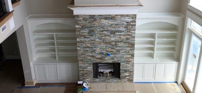 Fireplace with stone facade, built-in white bookshelves on both sides, and a large window to the right.