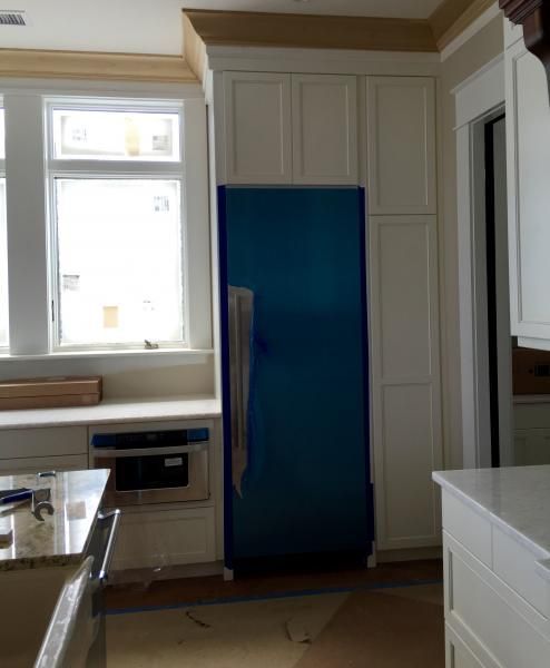 Kitchen with built-in white cabinets, a blue refrigerator, and a window. Light beige walls and wooden trim.