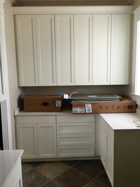 White cabinets in a kitchen, with countertops, and boxes resting on them.