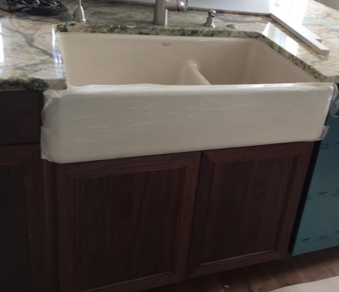 White farmhouse sink installed in a dark wood cabinet, with a granite countertop.