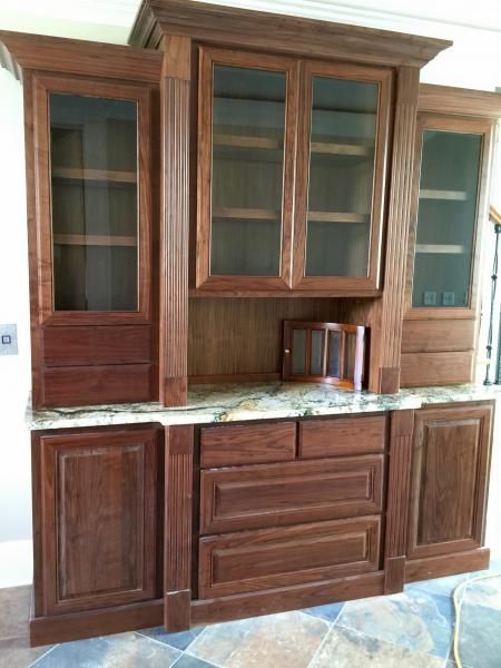 Wooden cabinet with glass-fronted upper section and granite countertop. Features doors, drawers, and shelving.