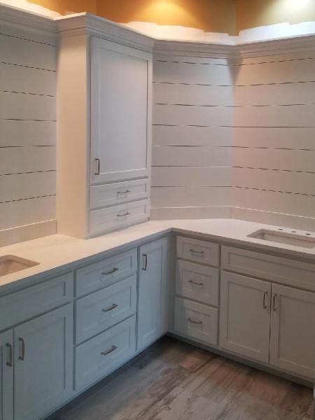 White cabinets and countertops in a corner kitchen with horizontal wood-paneled walls.
