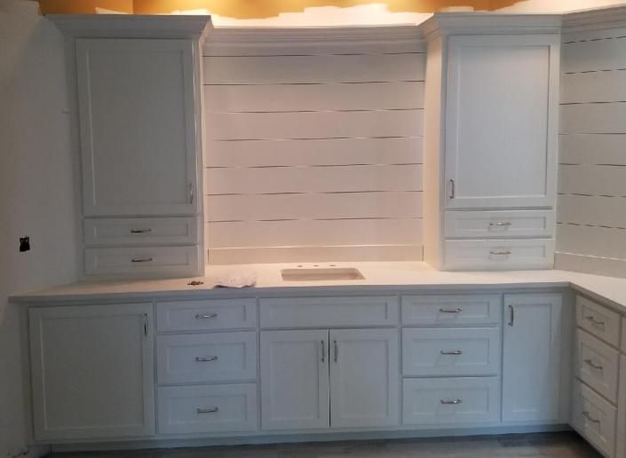 White cabinets in a kitchen, with a sink and drawers. Some cabinets are tall and wall-mounted.