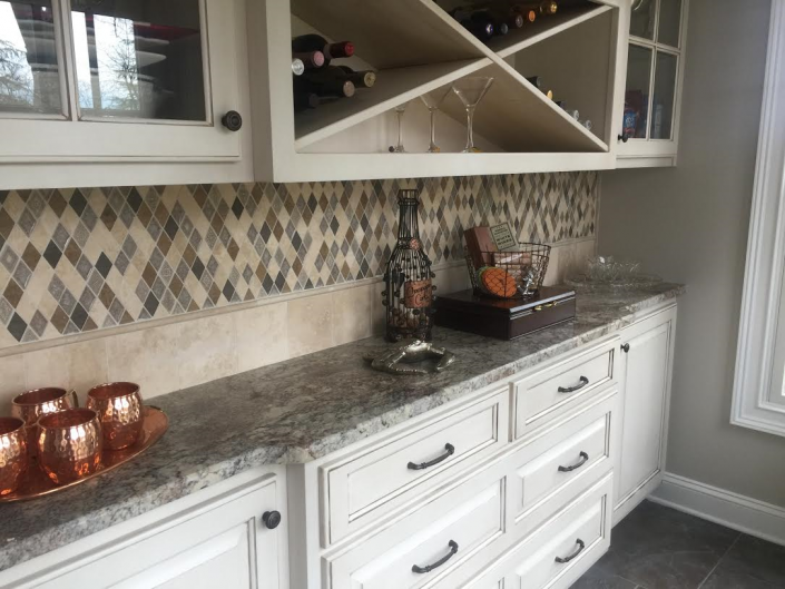 Kitchen cabinet and countertop with wine rack, drawers, and decorative backsplash and accessories.