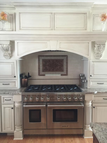 Stainless steel range and oven in a cream-colored kitchen with ornate cabinets.