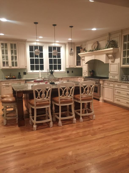 A well-lit kitchen with a dark island, light cabinets, wood floors, and bar stools.