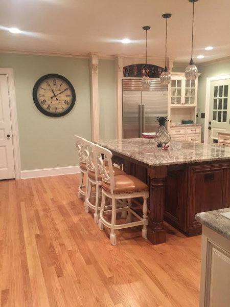 Kitchen with hardwood floors, island with seating, clock on wall, and recessed lighting.