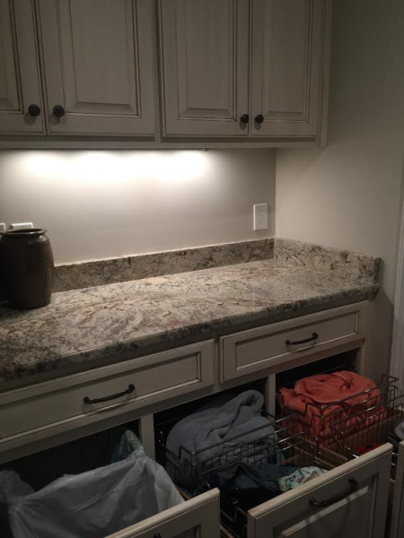 Laundry room with cream cabinets, granite countertop, and pull-out drawers holding laundry baskets and folded clothes.