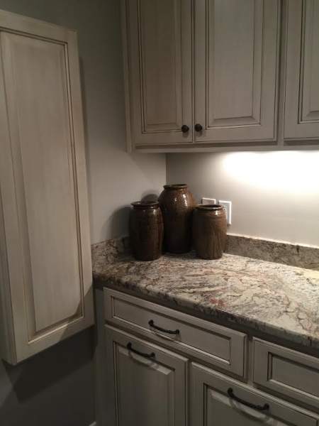 Cream-colored kitchen cabinets with a countertop and three brown jugs. Under-cabinet lighting.