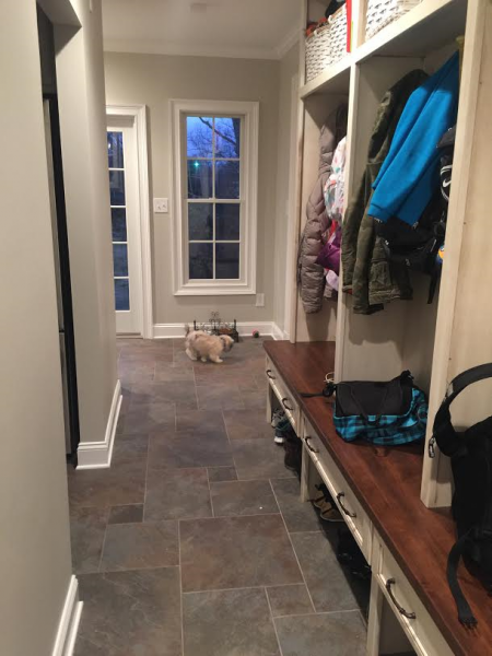 Hallway with coat rack, bench, and dog. Dark tile floor, neutral walls, and natural light.