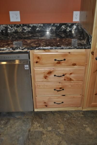 Kitchen cabinets with four drawers next to a dishwasher and granite countertop.