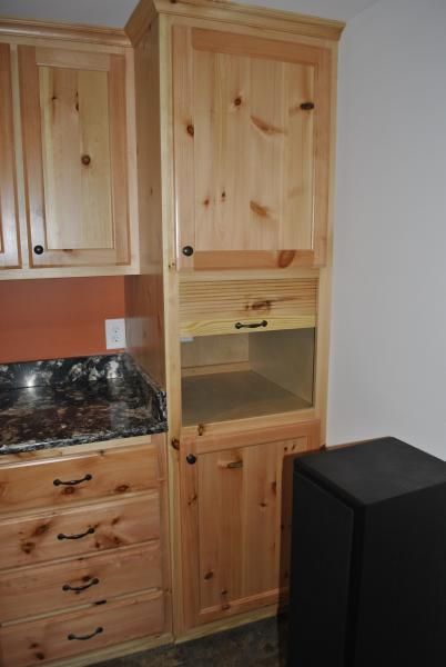 Wooden kitchen cabinets with granite countertop. Tall cabinet with open section, black speaker beside.
