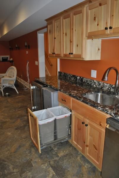 Kitchen with wooden cabinets, granite countertops, and a pull-out trash/recycling bin; orange wall.