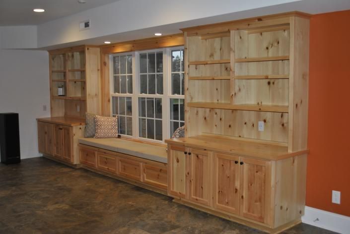 Built-in wooden cabinetry with window seat, shelves, and cabinets in a room with orange and white walls.