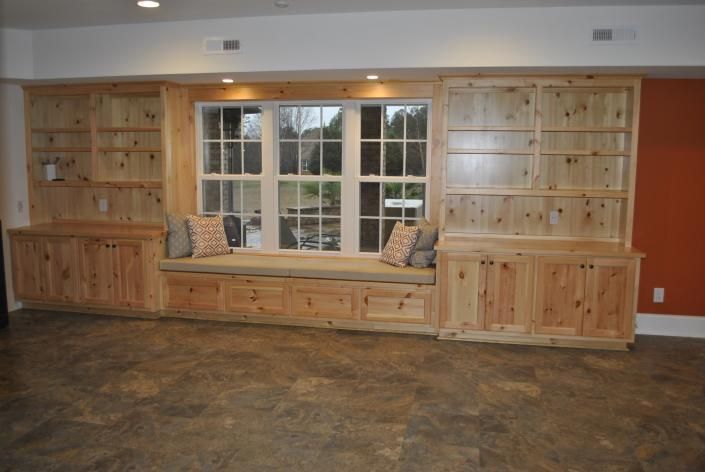 Built-in wooden window seat with cabinets and bookshelves. Window overlooks outdoors. Orange wall on the right.