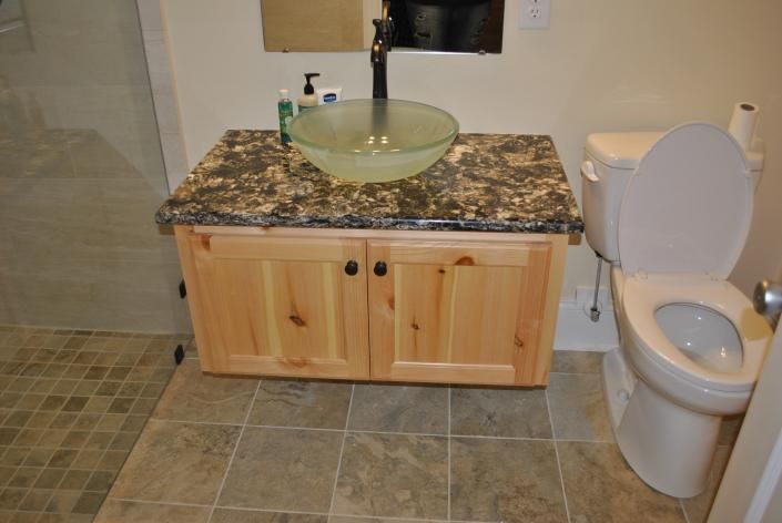 Bathroom with light wood vanity, granite countertop, glass bowl sink, and toilet.