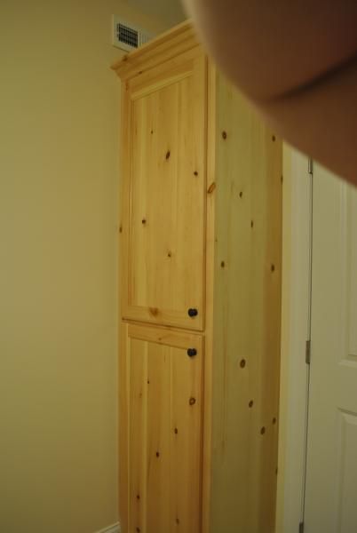 Tall, unfinished wooden cabinet with two doors against a beige wall.