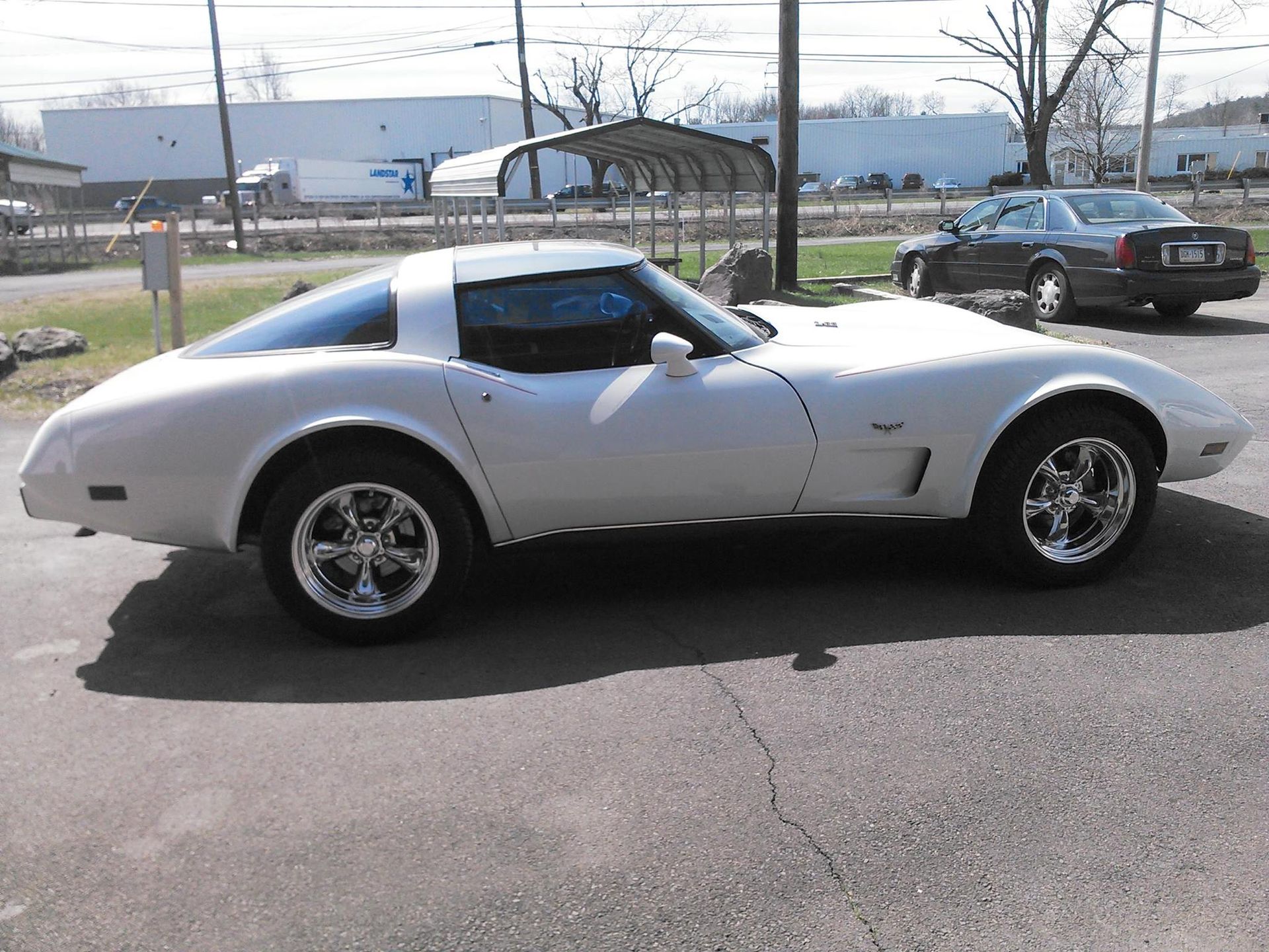 A white C3 Chevrolet Corvette parked on an asphalt lot on a sunny day.