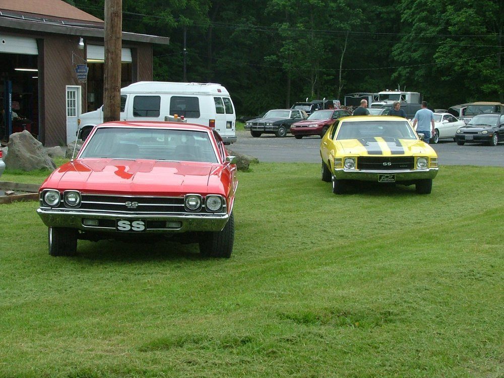A red classic Chevrolet SS and a yellow Chevrolet SS parked on a grassy lawn in front of a building.