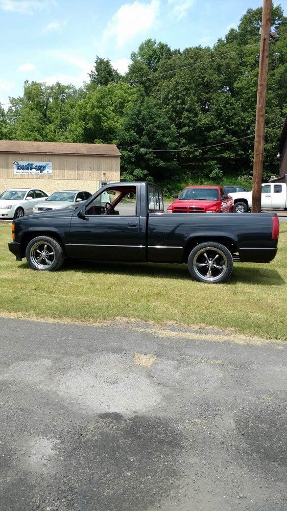 A black pickup truck parked on grass in front of a building with trees in the background.