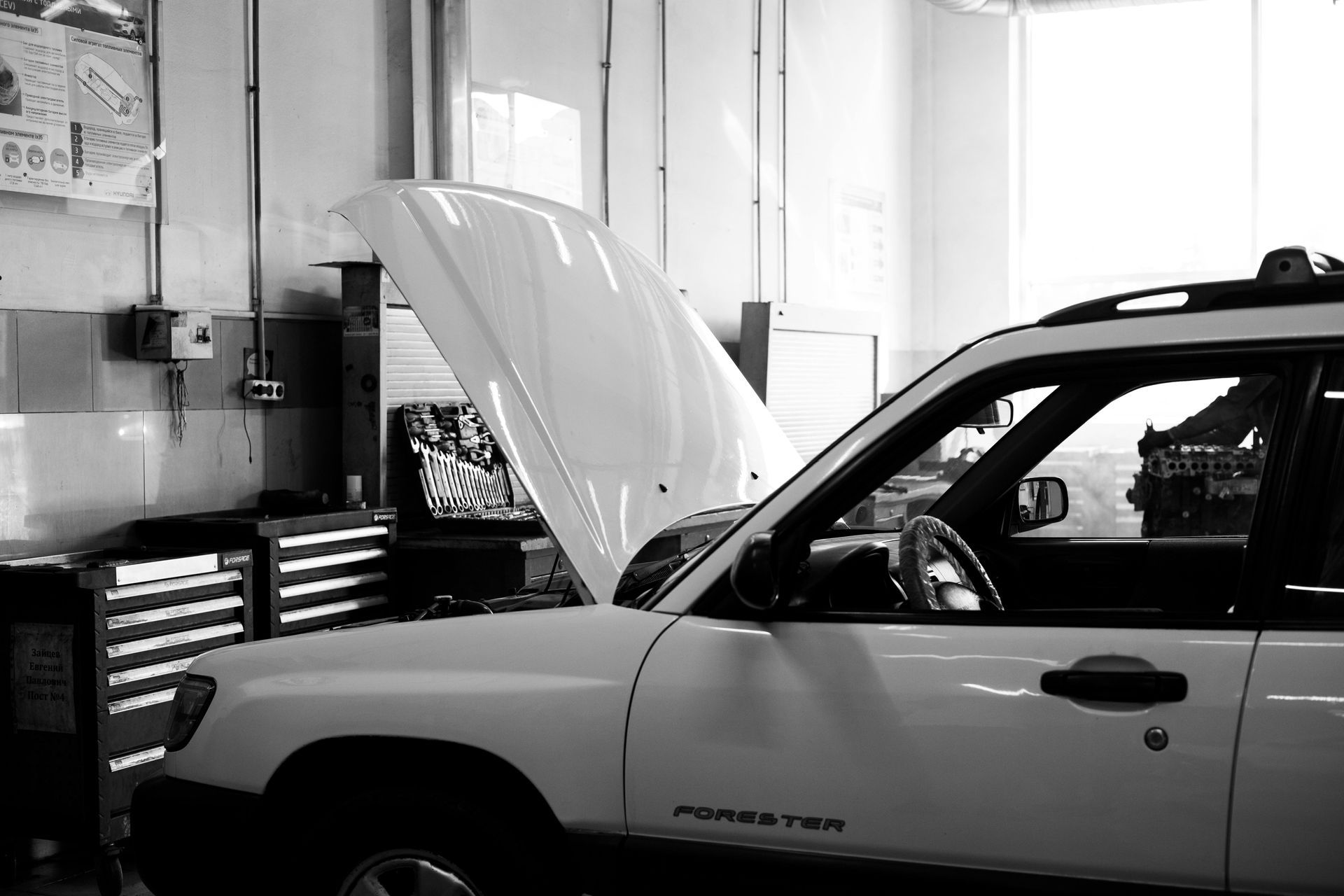 A white SUV with its hood open, parked inside a brightly lit automotive repair shop.