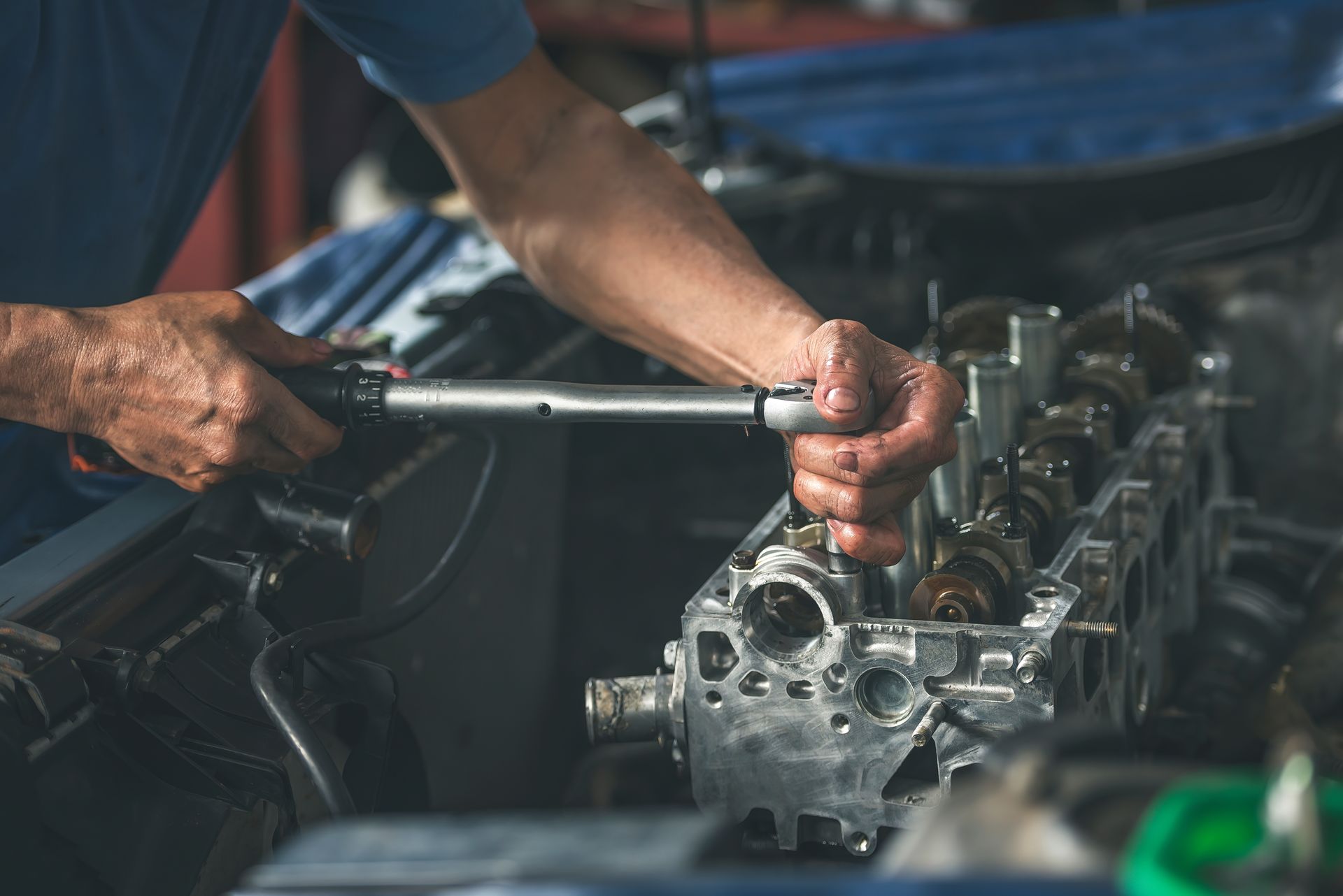 A mechanic uses a torque wrench to tighten a bolt on a disassembled car engine in a garage.