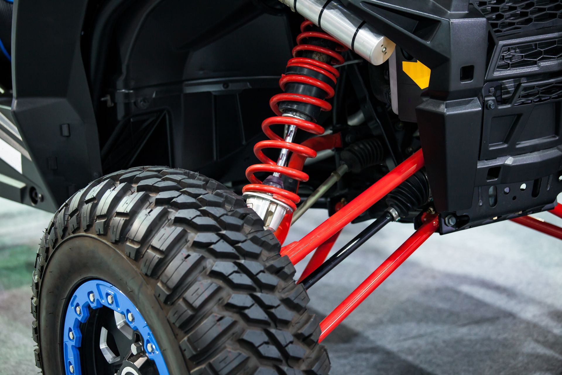 Close-up of a rugged off-road vehicle's front suspension, featuring a bright red coil spring and control arms.