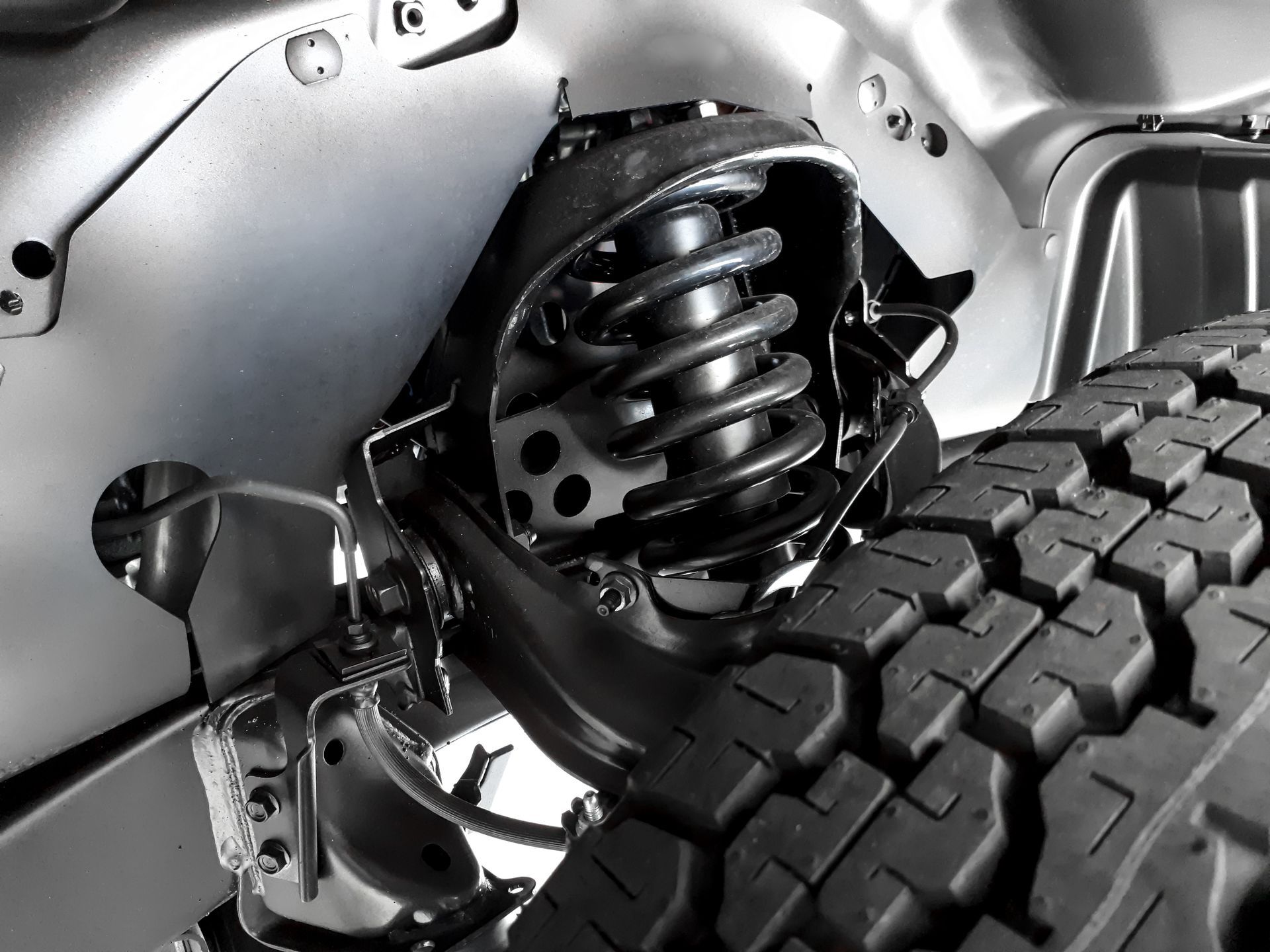 A close-up view of a vehicle's front suspension system, featuring a black coil spring and tire inside the wheel well.