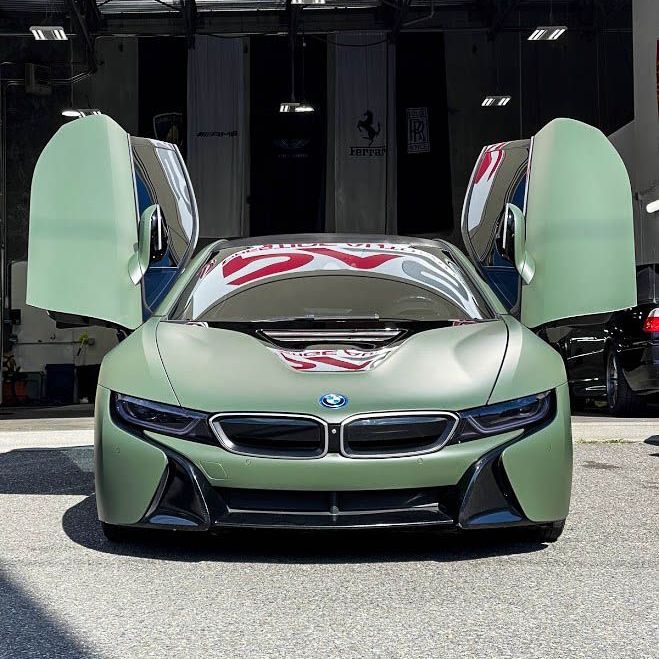 A green bmw i8 is parked in front of a building with its doors open.