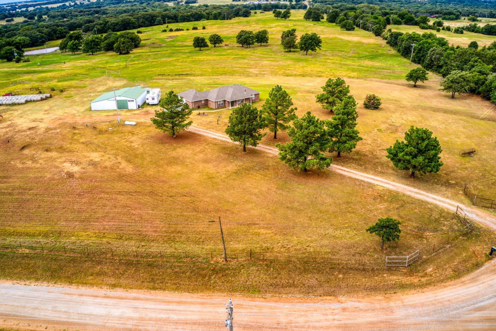 Aerial view of a rural property with a house, barn, and dirt road winding through grassy fields and trees.