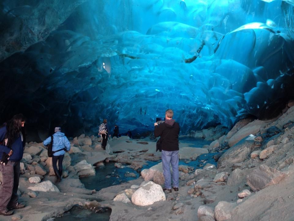 A group of people are standing in a cave taking pictures. Unique Juneau Tours
