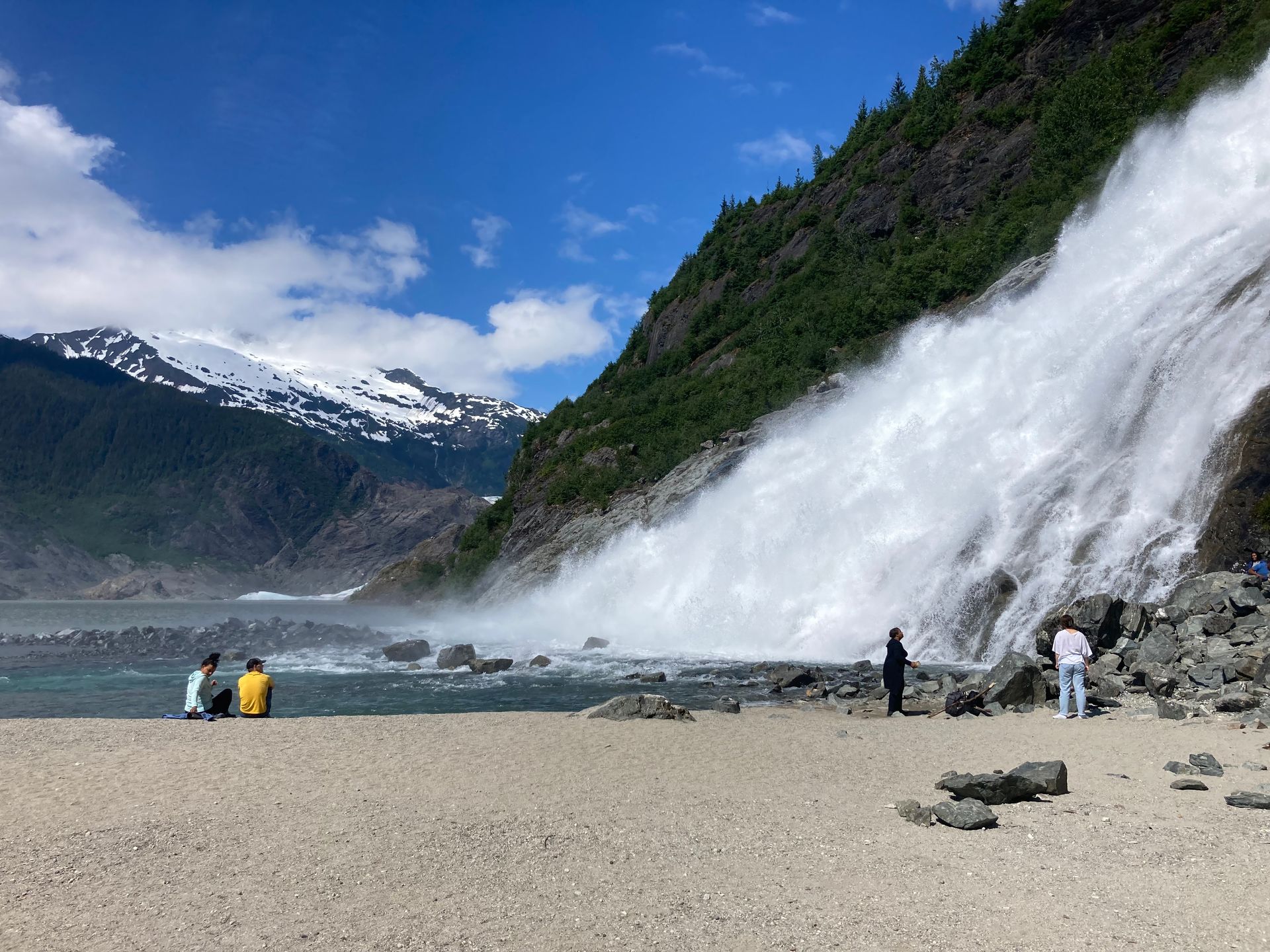 People are sitting on the beach near a waterfall in Juneau AK. Local Tour Guide in Juneau, AK. Unique Juneau Tours.
