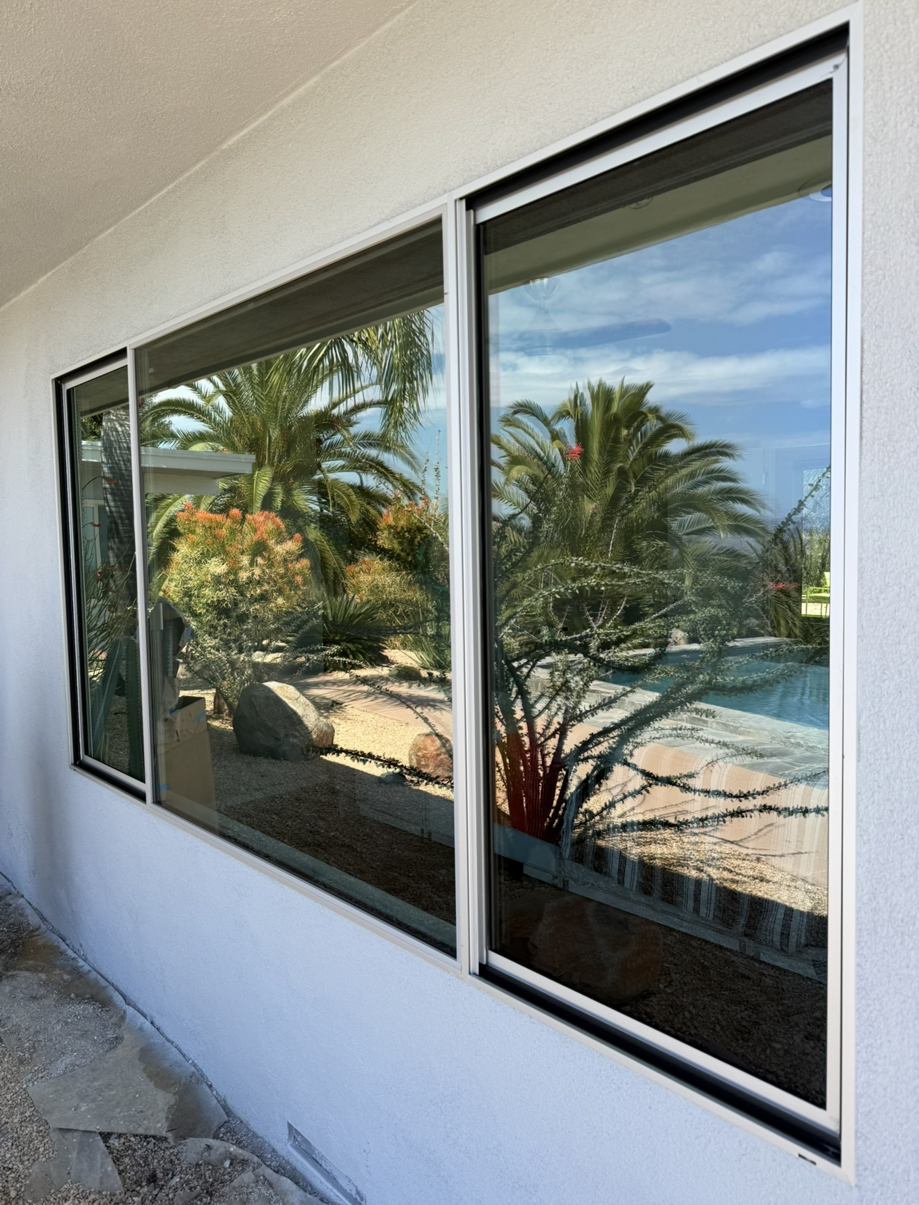 Three-panel window reflecting palm trees and a poolside patio with blue sky.