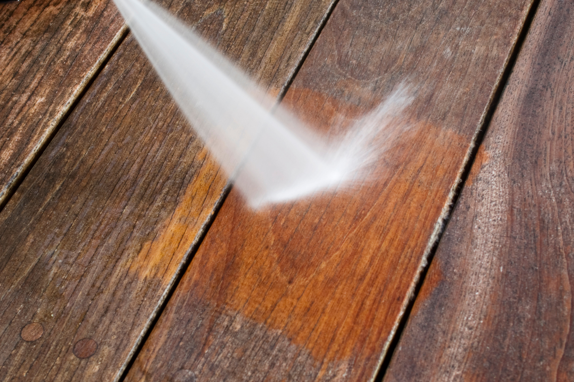 Pressure washing a wooden deck, cleaning a section of wet brown planks