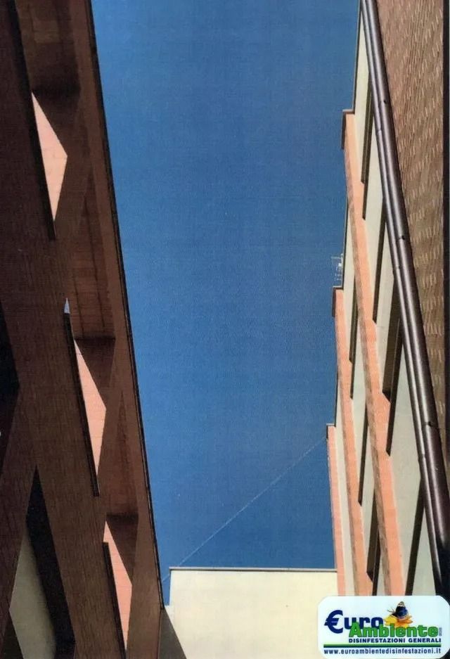 Vista ristretta del cielo azzurro tra alti edifici in mattoni, con una piccola insegna sul tetto in basso.
