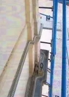 Primo piano di una piattaforma elevatrice blu da cantiere accanto a una parete di un edificio e ai telai delle finestre.