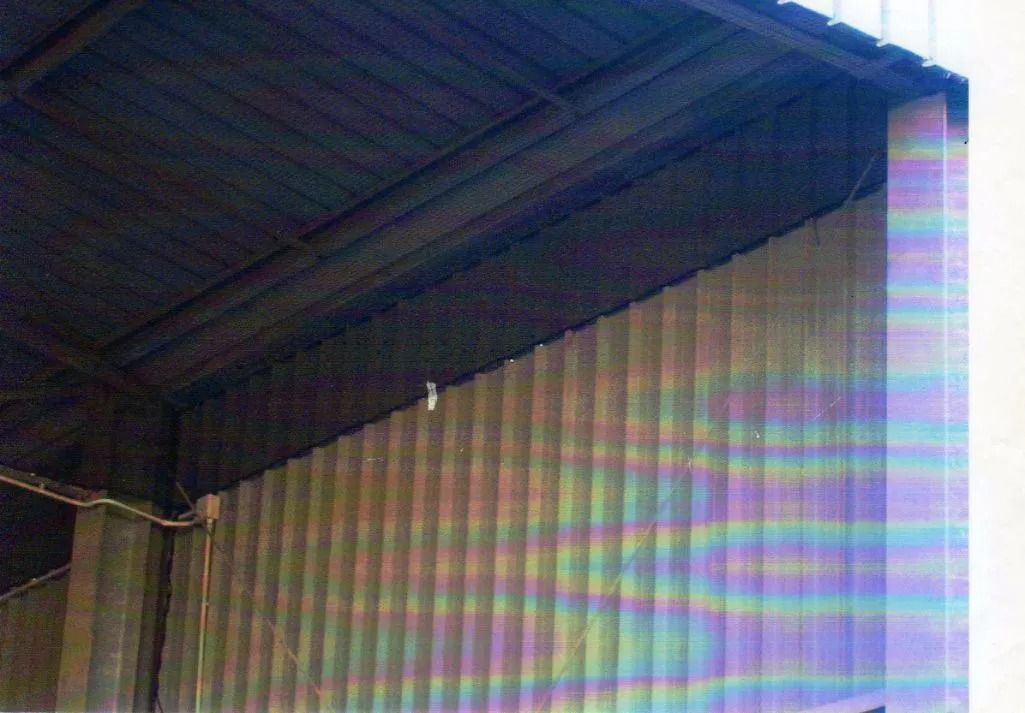 Tetto in lamiera ondulata sopra una parete color beige, che mostra l'angolo di un edificio industriale.