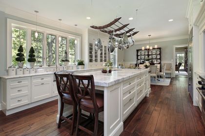 Bright kitchen with a large white island, dark wood floors, and hanging pot rack.