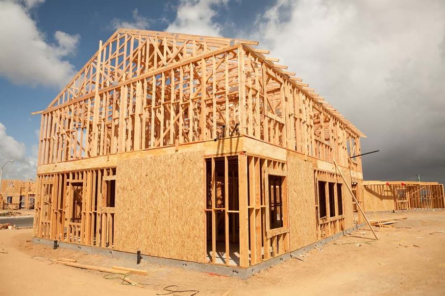 Wooden frame of a two-story house under construction against a cloudy sky.
