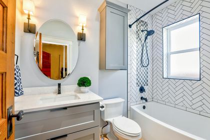 Bathroom with grey vanity, oval mirror, white and black tiled shower, and a white toilet.
