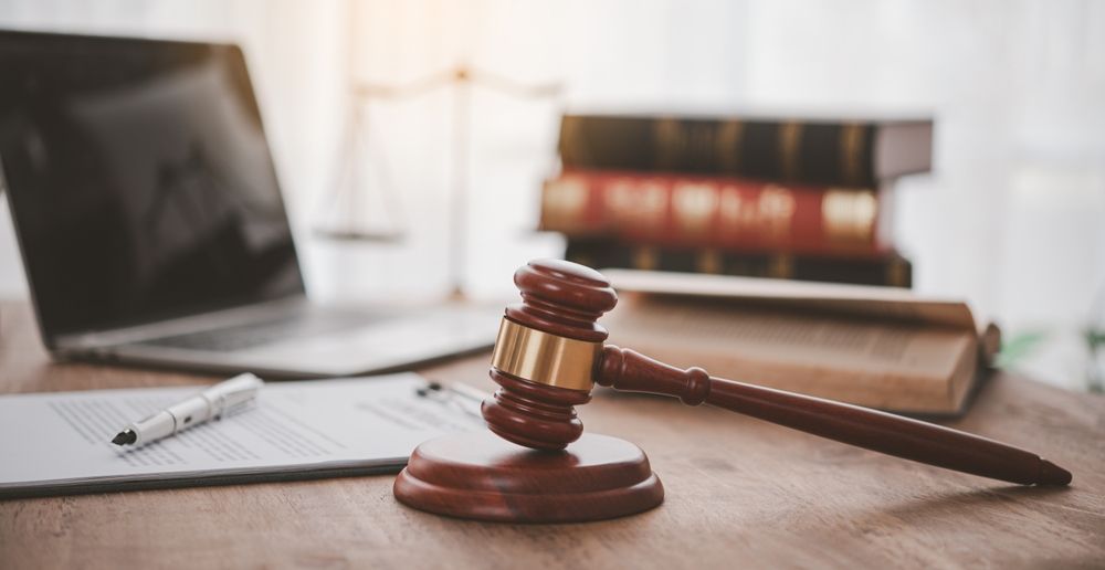Wooden gavel on desk with documents, laptop, and law books.