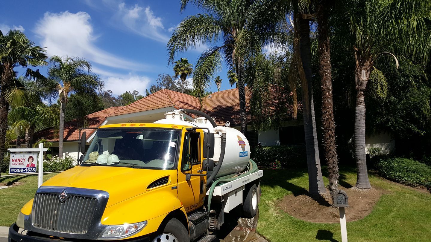 Yellow truck with a water tank parked in front of a house with a terracotta roof.