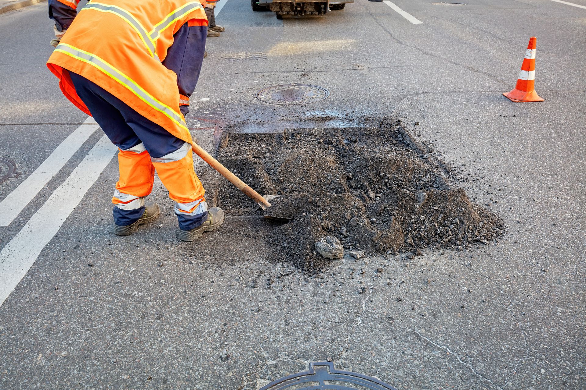 A man is digging a hole in the road with a shovel.
