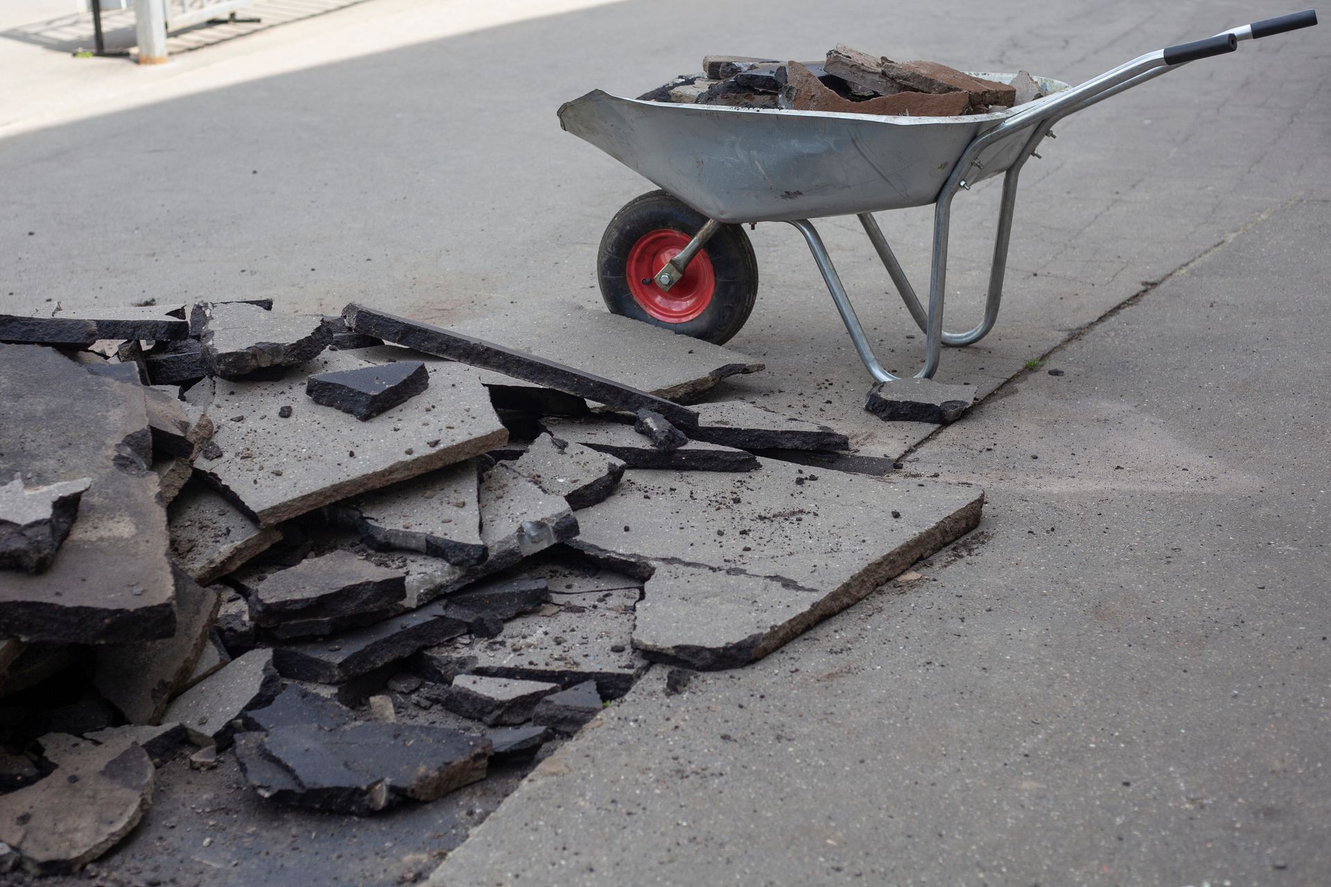 A wheelbarrow is sitting on the side of the road next to a pile of concrete.
