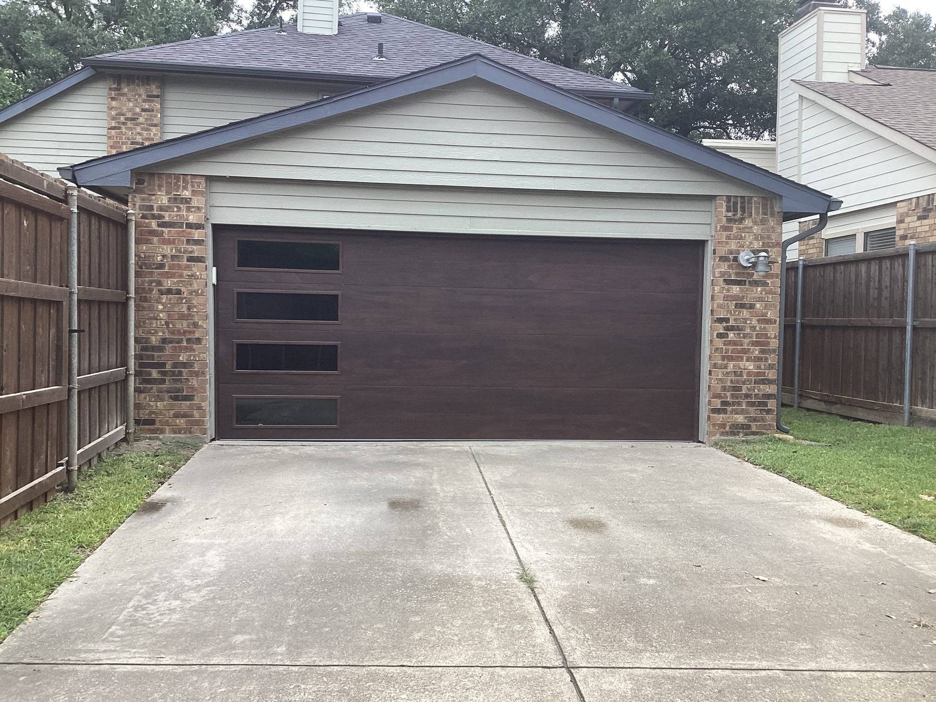 A suburban home with a dark brown garage door featuring four horizontal windows on the left, set against a concrete drive.